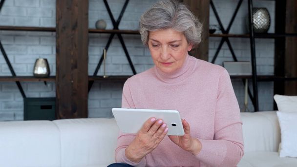 Elderly woman using a tablet gadget at home - Foto, imagen