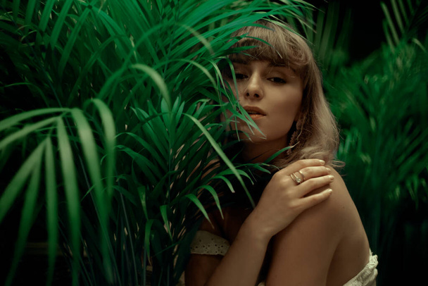 Woman in palm leaves. Model's face in green. Fashion photo of a girl in the tropics - Photo, Image