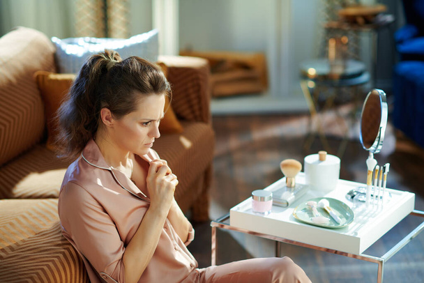 stressed stylish housewife in pajamas near table with toiletries at modern home in sunny winter day. - Foto, Imagem
