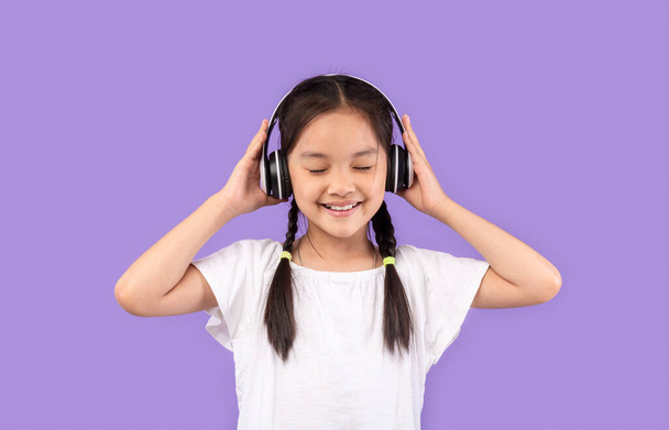 Menina japonesa em fones de ouvido desfrutando de música em fundo roxo - Foto, Imagem