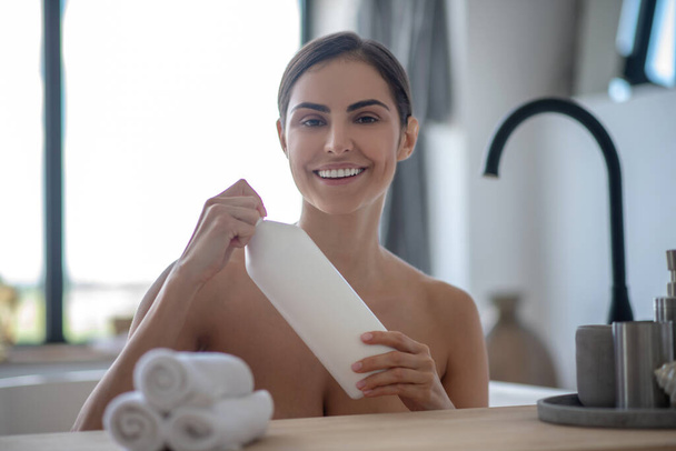 Woman holding a bottle with bath foam and smiling - Foto, Bild