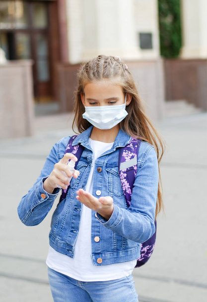 Little girl child with face mask and sanitizer. Education concept. Back to school after covid-19.  Preteen student disinfecting hands before school outdoors. - Photo, image