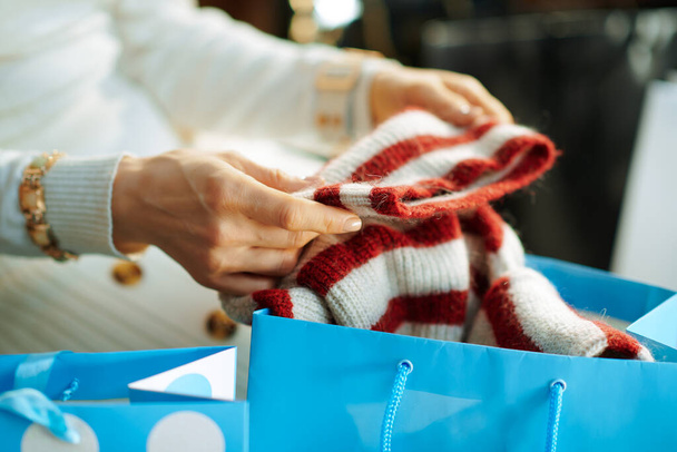 Closeup on trendy 40 years old housewife in white sweater and skirt with shopping bags checking purchased sweater in the modern living room in sunny winter day. - Foto, Imagen
