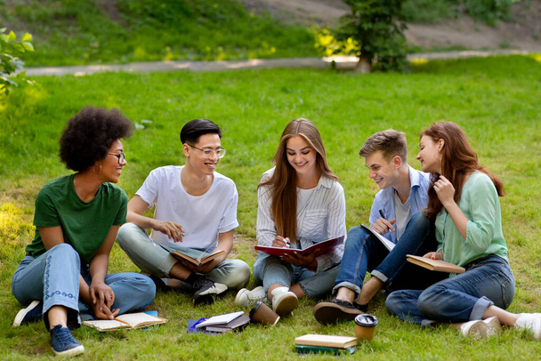 Concepto de aprendizaje. Grupo de amigos de la universidad que se preparan para las clases al aire libre, estudiando juntos - Foto, imagen