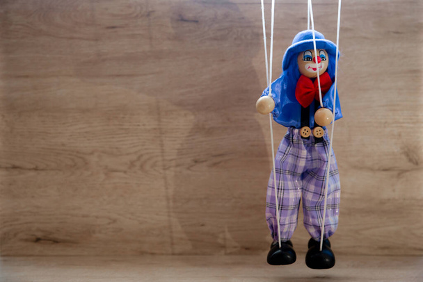 Eine Marionetten-Clown-Puppe, die an dünnen Fäden auf einem hölzernen Hintergrund hängt - Foto, Bild