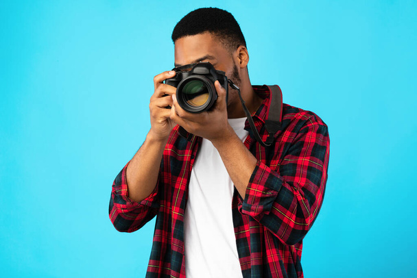 Fotógrafo afroamericano tomando fotos de pie sobre fondo azul - Foto, imagen