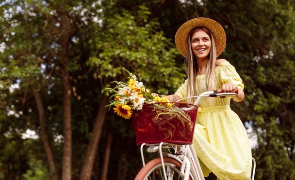 Charming young woman riding bicycle in nature - Фото, изображение