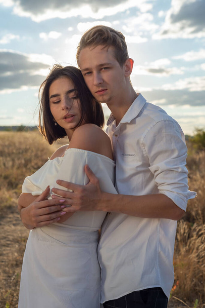 portrait of a young guy and a girl twenty two years old. Generation Z wedding. Against the backdrop of a cloudy sky, a setting sun in a field. - Photo, Image
