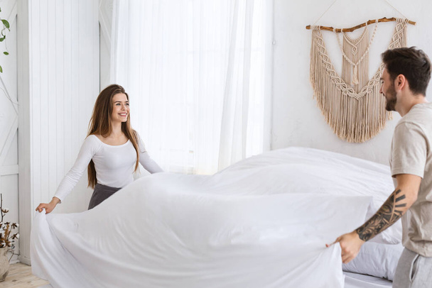 Limpia en el dormitorio. Sonriente joven hombre y mujer haciendo la cama por la mañana - Foto, imagen