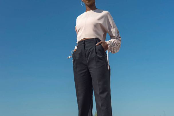 Closeup portrait fashionable dark skinned girl, African girl in a blouse and business pants, posing. Against the background of blue sky. Fashionable black girl, blacks fashion. young Nigerian girl, young African girl, twenty five years old, posing in - Фото, зображення