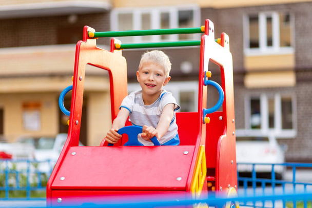 Счастливый мальчик 5-6 лет летом играет на детской площадке во дворе. Детский образ жизни - Фото, изображение