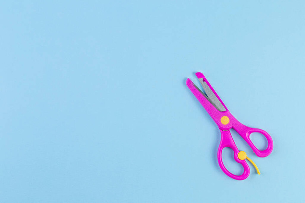 Minimalist photo of pink children's scissors on blue background. back to school concept with stationery. With copy space, template for text or design. Top view, Flat lay - Fotó, kép