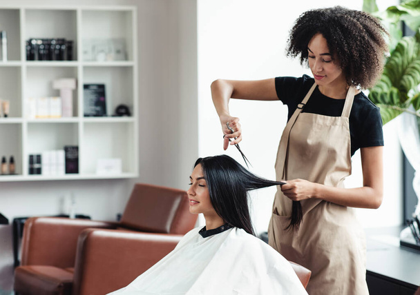 Nuori musta kampaaja leikkaus hiukset naispuolinen asiakas salonki - Valokuva, kuva