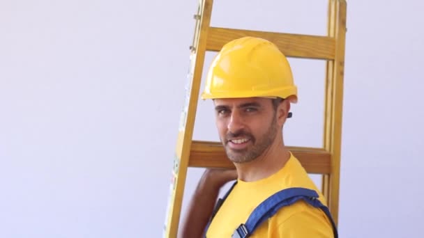 Builder with worker cloths stand on a ladder - Imágenes, Vídeo