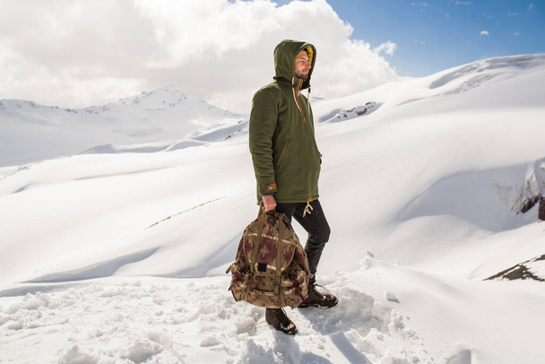 jonge hipster man wandelen in de bergen, wintervakantie reizen, noorden, sneeuw, warme kleren, rugzak, anorak, jeans, laarzen - Foto, afbeelding