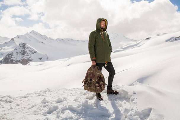 young hipster man hiking in mountains, winter vacation traveling, north, snow, warm clothes, backpack, anorak, jeans, boots - Zdjęcie, obraz