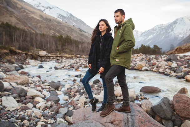 young beautiful hipster couple in love, walking by the river, wild nature, winter vacation, hiking, traveling together, backpacker, warm clothes, jacket, romance - Foto, immagini