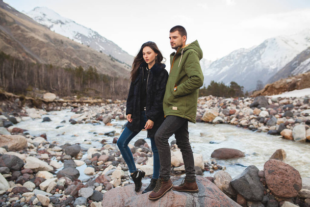 young beautiful hipster couple in love, walking by the river, wild nature, winter vacation, hiking, traveling together, backpacker, warm clothes, jacket, romance - Fotó, kép