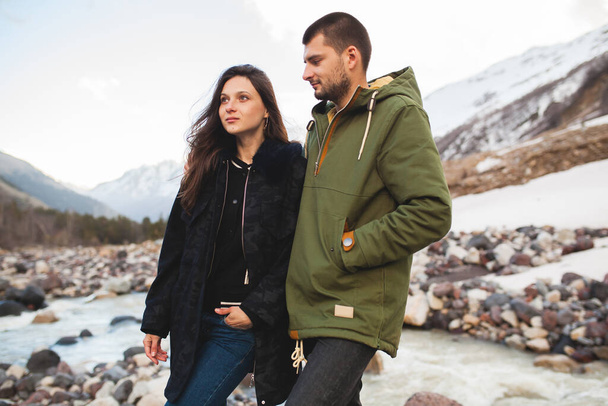 young beautiful hipster couple in love, sitting by the river, wild nature, winter vacation, hiking, traveling together, backpacker, warm clothes, jacket, romance - Foto, immagini