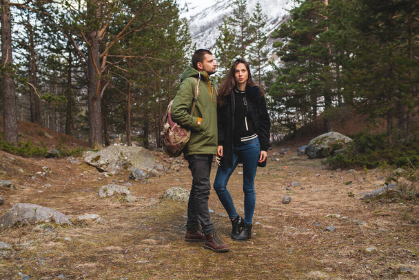 young beautiful hipster man and woman in love traveling together in wild nature, hiking in forest, autumn style apparel, coat, romance, vacation, warm clothes - Фото, зображення