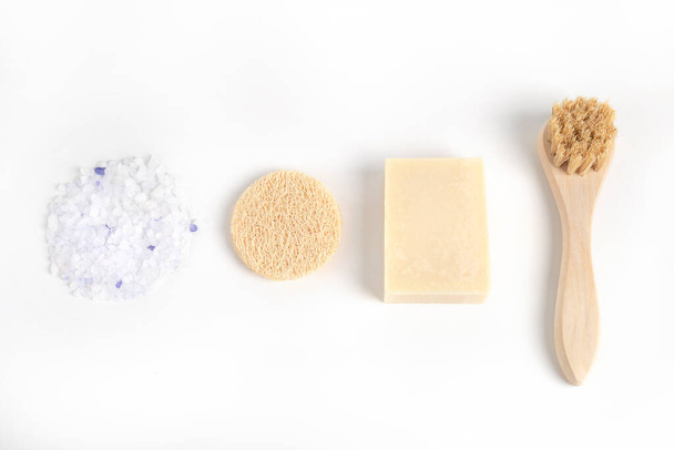 Face cleansing tools. Wood natural brush, handmade soap bar, facial organic sponge and large crystals of sea salt. Home or salon spa procedures and self care concept - 写真・画像