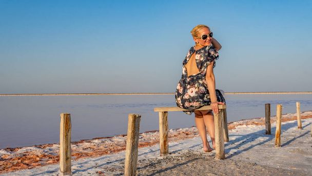 Smiling young woman in a beautiful dress with gentle lips against a salty background like winter on a lake with blue clouds in hot sunny weather - Foto, afbeelding