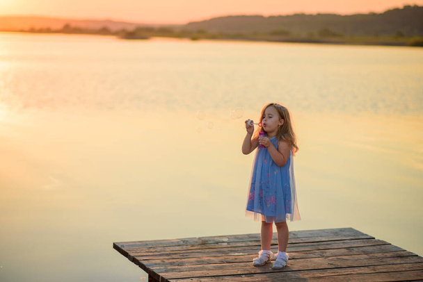 Ein kleines Mädchen bläst Blasen auf der Seebrücke am See. - Foto, Bild