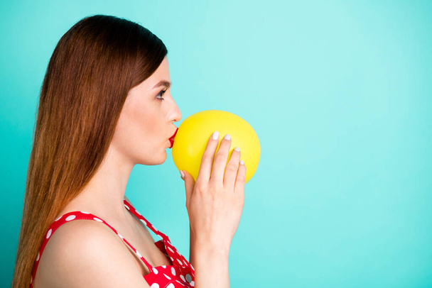 Profile photo of attractive lady look side empty space hold helium air balloon inside mouth breathe in talk funny voice wear red dotted retro dress singlet isolated teal color background - 写真・画像