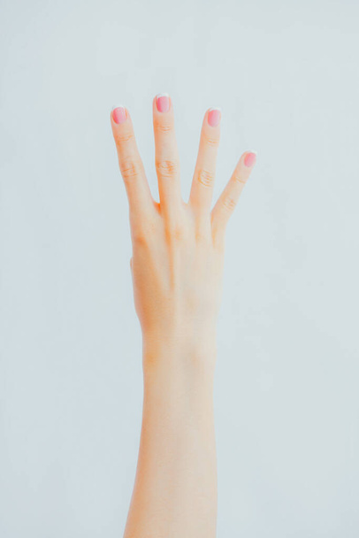 Woman's hand shows four fingers on gray background - Photo, image
