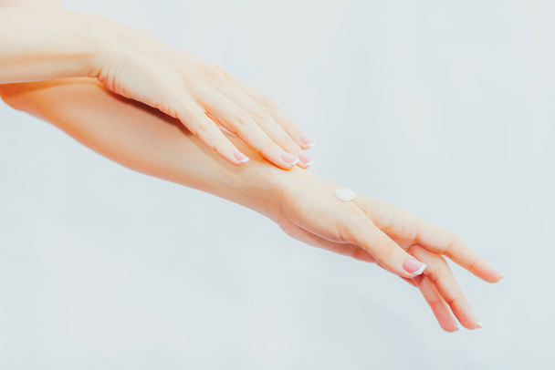 Kobieta z francuskim manicure nakłada krem na ręce. Pielęgnacja i masaż dłoni. Ręce do góry. - Zdjęcie, obraz