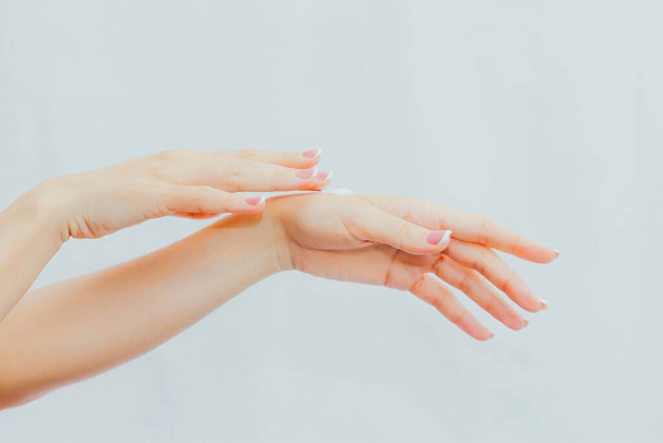 Woman with french manicure applies cream to her hands. Hand skin care and massage. Hands close up - Φωτογραφία, εικόνα