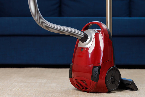 Red vacuum cleaner on a beige carpet - Fotó, kép