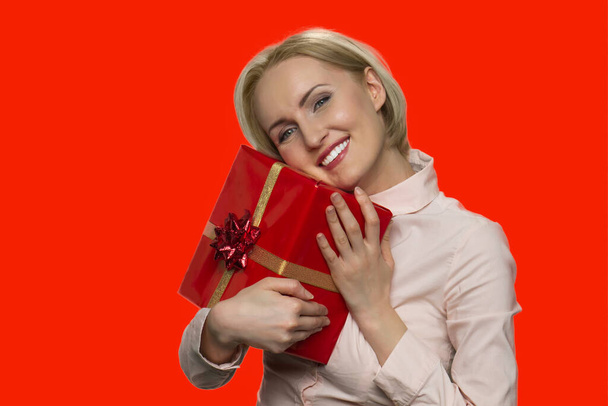 Happy woman hugging gift box on red background. - Фото, изображение