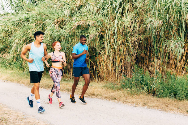 Üç arkadaş dışarıda egzersiz yapıyor, kırsal alanda koşuyor. - Fotoğraf, Görsel