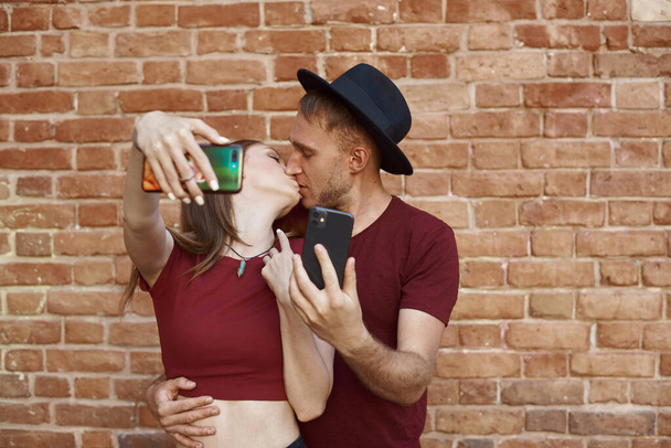 A couple is kissing for a selfie. The young man and woman makes selfie. - Photo, Image