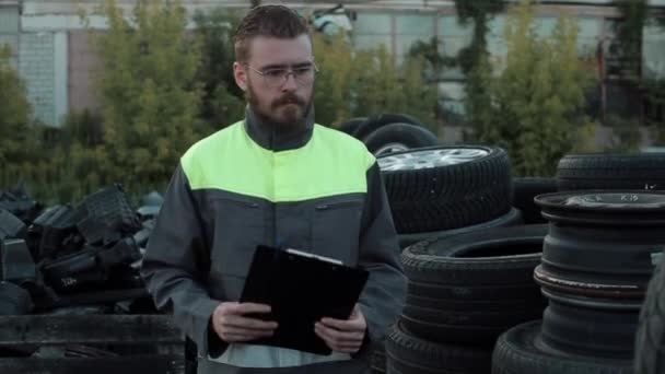 制服を着た若い髭を生やした自動車整備士が修理工場の庭に立っていて、カメラに何か言っている。閉鎖 - 映像、動画