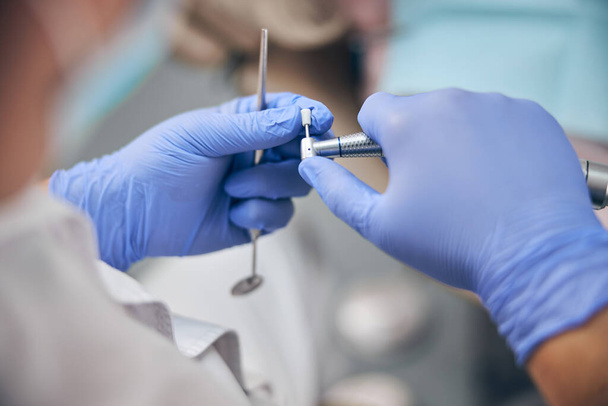 Доктор в синіх рукавичках тримає стоматологічне обладнання в руках
 - Фото, зображення