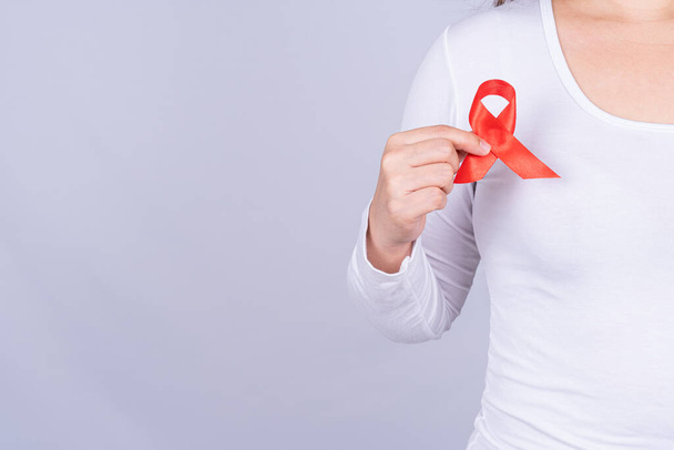 Red AIDS awareness ribbon holding by man on grey background. World Aids Day, Healthcare and medical concept. - Photo, Image