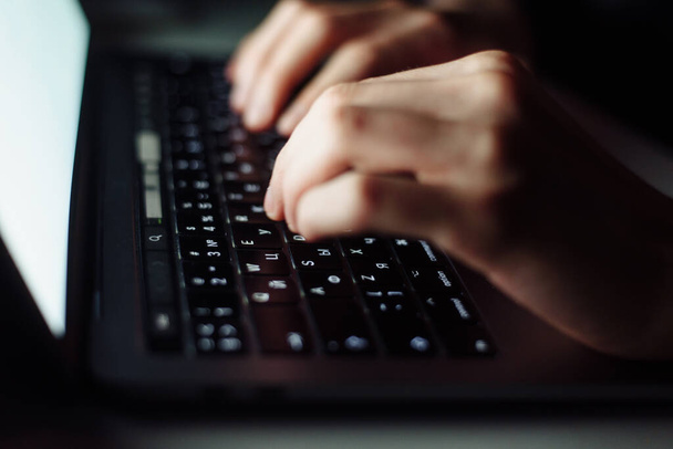 Закройте рукописную клавиатуру человека на ноутбуке в темной операционной, концепция кибербезопасности. Хакер с помощью ноутбука. - Фото, изображение