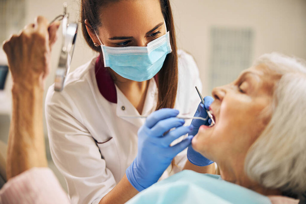 Retrato de una dentista que trata los dientes de una paciente anciana - Foto, imagen
