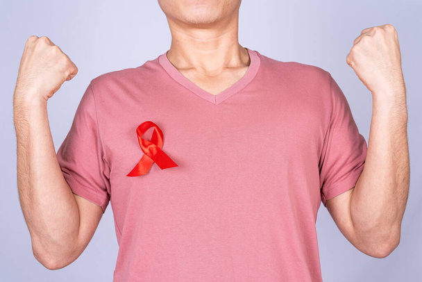 Kızıl AIDS farkındalık kurdelesi gri arka plandaki adamın elinde. Dünya Yardım Günü, Sağlık ve Tıbbi Konsept. - Fotoğraf, Görsel