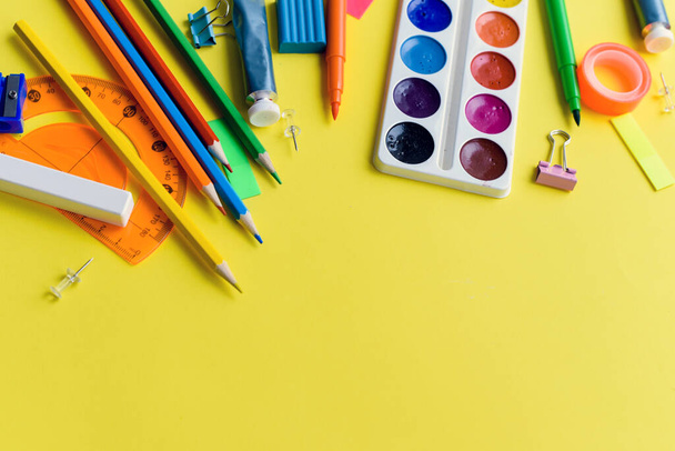 Pittura, matite e forbici. Accessori scolastici su sfondo giallo. Vista dall'alto. - Foto, immagini