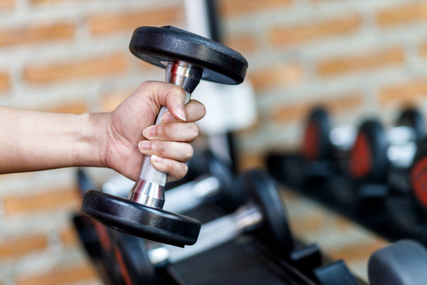 Closeup a man's hand holds a dumbbell with his right hand in the gym, Concept for exercise and health care. - 写真・画像