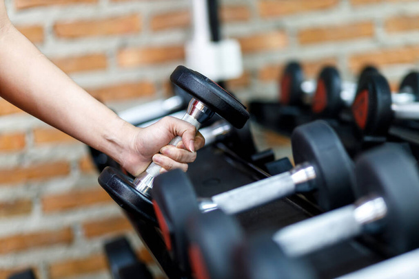 Closeup a man's hand holds a dumbbell with his right hand in the gym, Concept for exercise and health care. - 写真・画像