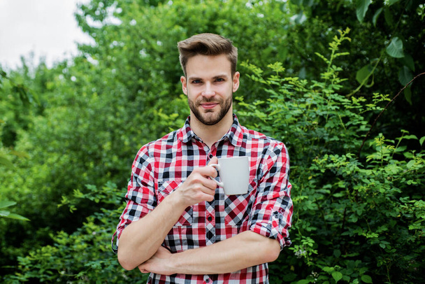 good morning. fresh inspiration and energetic beverage. handsome bearded guy drinking tea outdoor. he loves cocoa. food and drink. cheerful man in checkered shirt drink morning coffee - Foto, Imagen