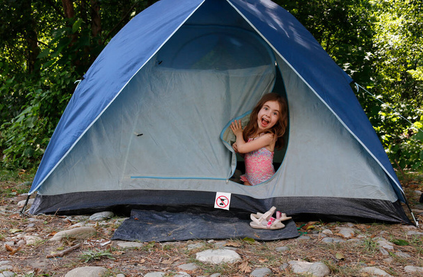 Portrait de petite fille émotionnelle assise à l'intérieur d'une tente et regardant la caméra. Enfant grimaçant. - Photo, image