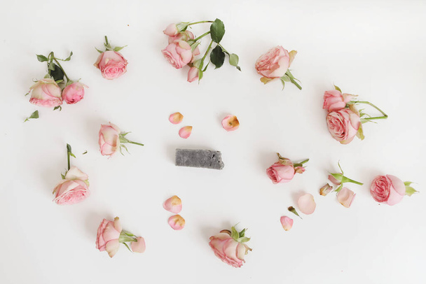 Natuurlijke zelfgemaakte biologische zeep met roze rozen en bloemblaadjes op witte achtergrond. Spa-concept, bovenaanzicht, plattegrond  - Foto, afbeelding