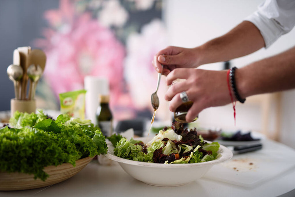 close-up of hands, man puts sauce in  salad, healthy food, green salad, selective focus - Photo, image