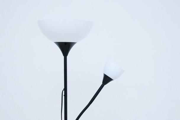 Electric floor lamp in black with white lampshades in the interior of the room against the background of a white wall. - Fotó, kép
