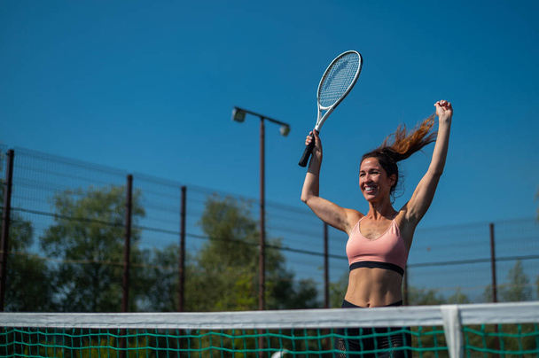 Χαμογελαστή γυναίκα νικήτρια στο τένις. Ευτυχισμένο κορίτσι σε ένα υπαίθριο γήπεδο τένις. - Φωτογραφία, εικόνα